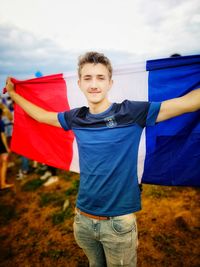 Portrait of young man holding french flag while standing on field