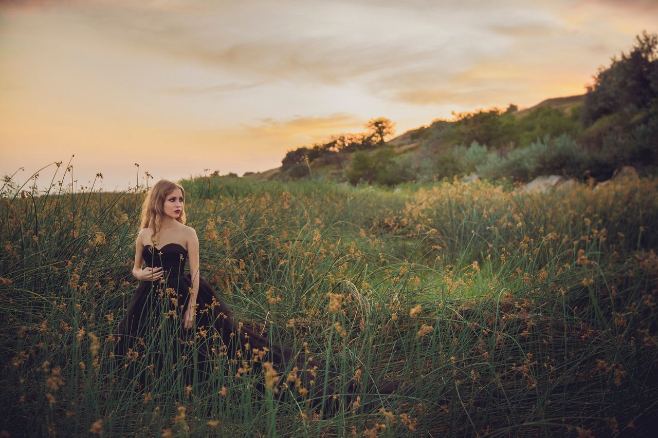 sky, plant, sunset, land, one person, field, leisure activity, grass, nature, lifestyles, real people, beauty in nature, cloud - sky, young adult, young women, landscape, casual clothing, growth, outdoors