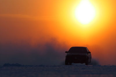 Car on snowy landscape against orange sky during sunset