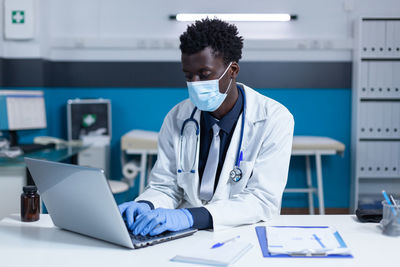 Doctor wearing mask using laptop in clinic