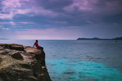 Man standing on rock by sea against sky