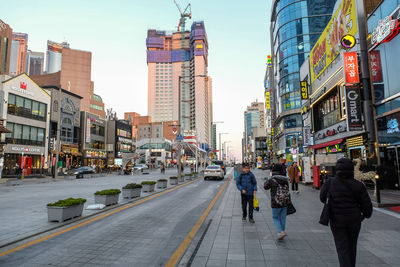 People walking on road by buildings against sky in city