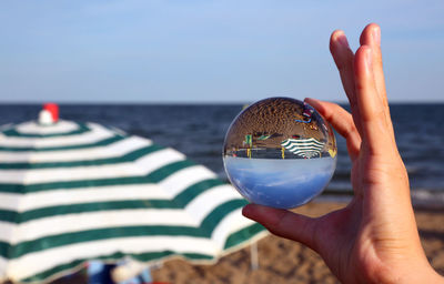 Close-up of hand holding crystal ball against sea