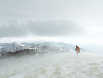 Hiker standing on snowcapped mountain against sky