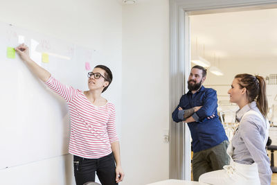 Businesswoman explaining adhesive note to colleagues in creative office