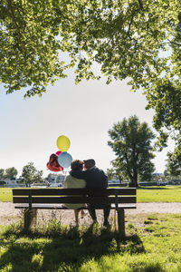 Happy senior couple with balloons kissing on bench in a park