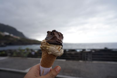 Hand holding ice cream cone against sea