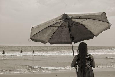 Rear view of woman standing below parasol at beach