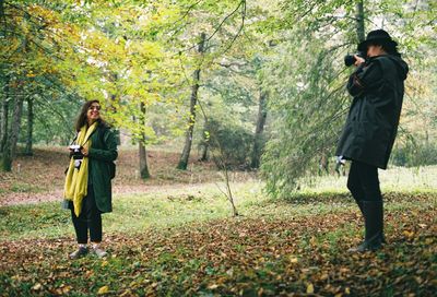 Full length of man photographing woman standing in forest
