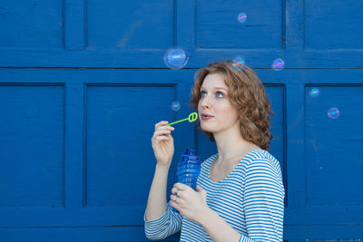 Playful woman blowing bubbles while standing against door