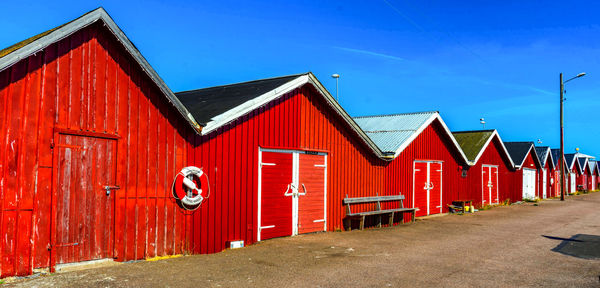 Red barn in row by houses against clear blue sky