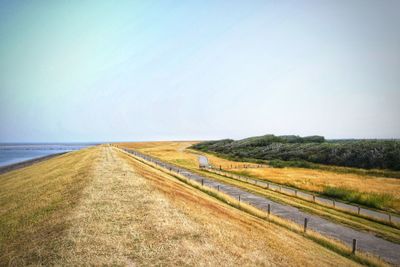 Road leading towards agricultural field against sky
