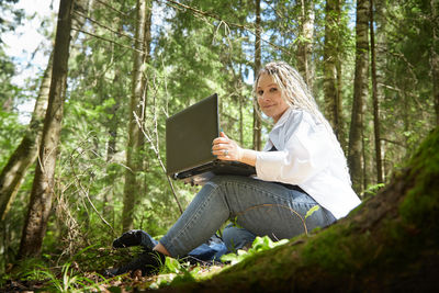 Portrait of young woman using digital tablet while standing in forest