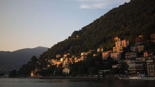 Illuminated city by mountains against sky