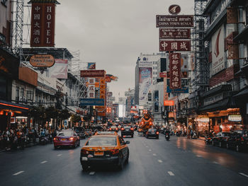 Cars on city street by buildings against sky