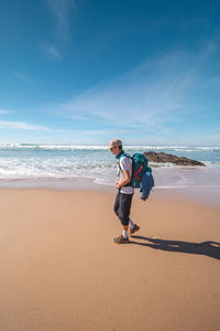 Rear view of woman standing at beach against sky