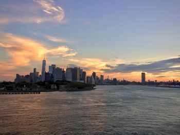 Sea by buildings against sky during sunset