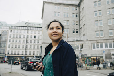 Side view of confident female entrepreneur with phone standing in city