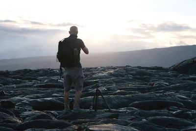 Rear view of man with tripod standing on volcanic landscape against sky at hawaii volcanoes national park