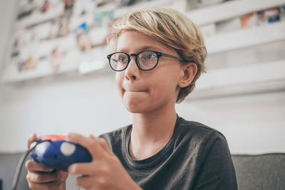 Boy wearing eyeglasses playing video games with joystick at home