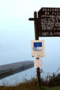 Information sign by sea against sky