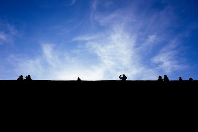 Low angle view of silhouette people against blue sky