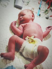 High angle view of shirtless newborn baby boy lying on bed in hospital