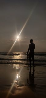 Silhouette man standing on beach against sky during sunset