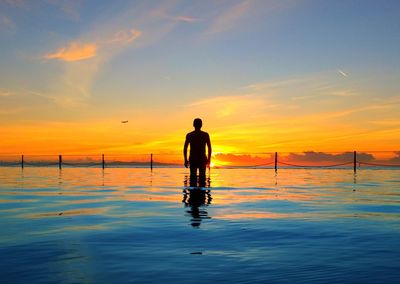 Silhouette man standing in sea against sky during sunset