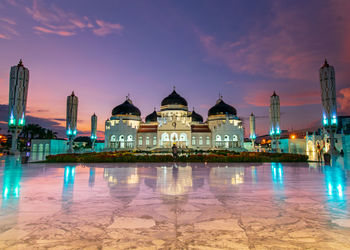 View of illuminated building with reflection on marble floor against sky at dusk