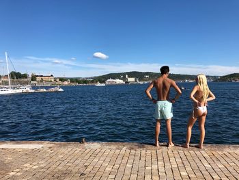 Rear view of the scandenavian couple on swimming suits standing on ocean against sky in summer