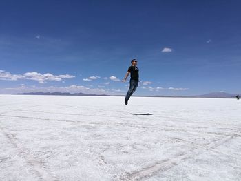 Young man levitating on salt flat against blue sky at salar de uyuni