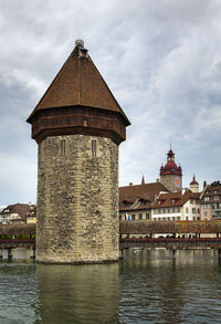 Old building by river against cloudy sky