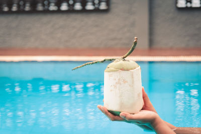 Person holding ice cream against swimming pool