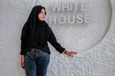 Portrait of young woman standing against wall