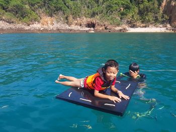 Smiling boy on diving platform by father in sea