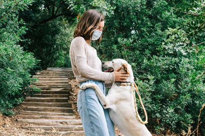 Young woman wearing a face mask caressing a dog playing in the park. concept of new normal outdoors.