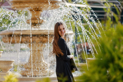 Smiling woman standing against water fountain