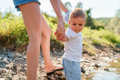 Low section of woman holding son hands at lakeshore
