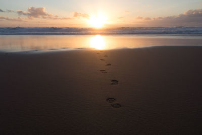 Footprints on sea shore against sky during sunset
