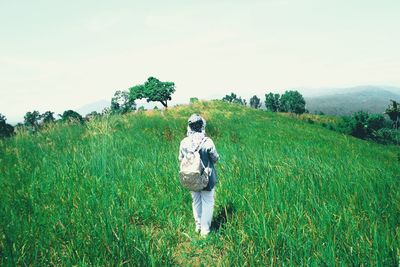 Rear view of woman with backpack standing on field against sky