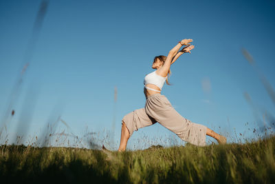 Young woman practicing yoga outdoors in the field with blue sky on the background	
