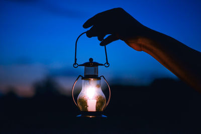 Close-up of hand holding illuminated lantern against sky at night