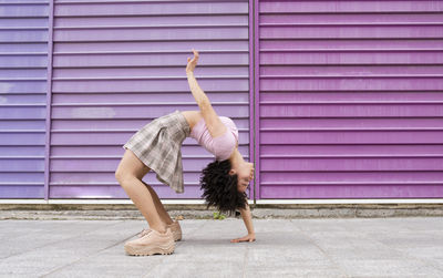 Female young dancer bending over backwards by colorful wall