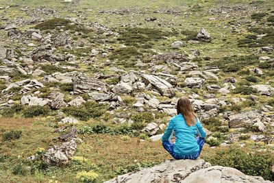 Rear view young woman in sitting on stone in mountain meditation in nature, consciousness