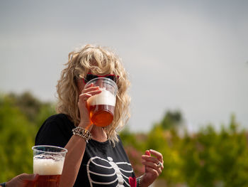 Cropped hand of man and woman drinking beer in glass against sky