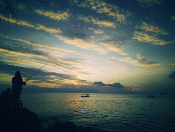 Silhouette fishing rod on sea against sky during sunset