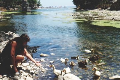 Side view of woman sitting on rock by lake