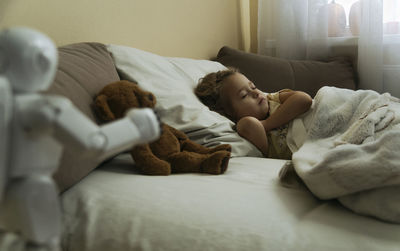Portrait of cute little girl sleeping in bed with toy bear and toy robot in the foreground
