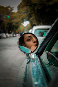 Portrait of young man reflecting on side-view mirror while traveling in car